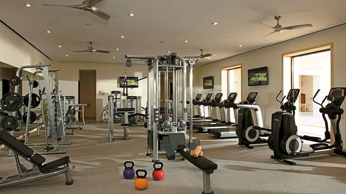 Fitnessstudio im Hotel Secrets Akumal Riviera Maya mit verschiedenen Trainingsgeräten und Fernsehern.