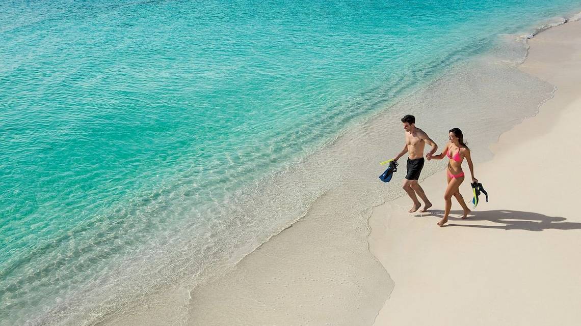 Ein Paar mit Schnorchelausrüstung läuft am Strand des Secrets Akumal Riviera Maya.