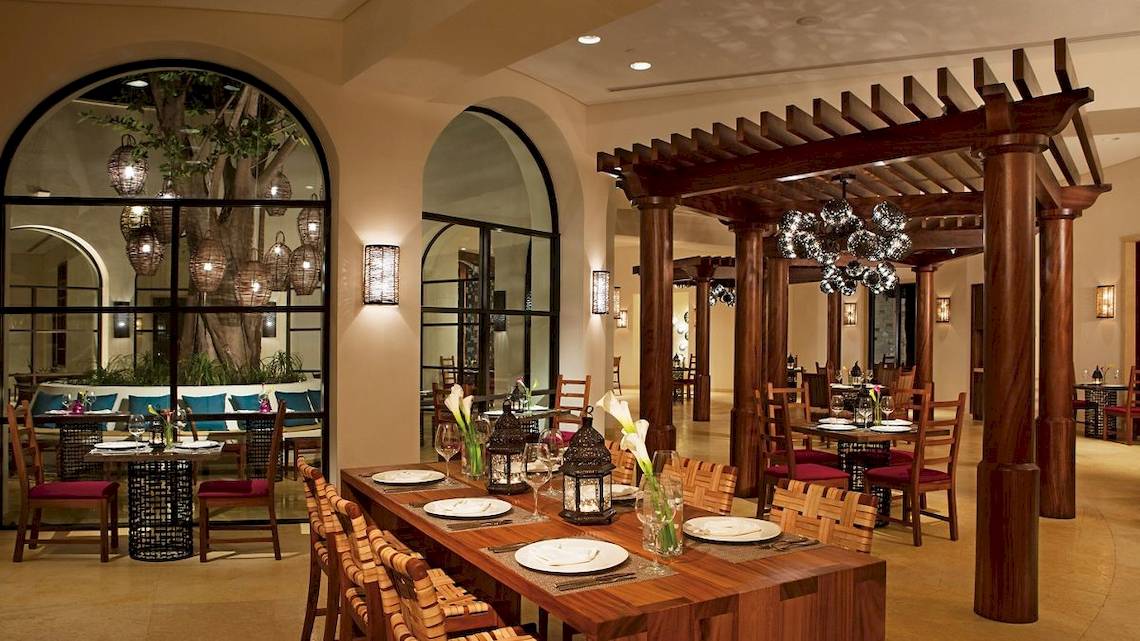 Innenansicht des Restaurants im Secrets Akumal Riviera Maya Hotel mit Holztischen, Stühlen und einer Pergola.