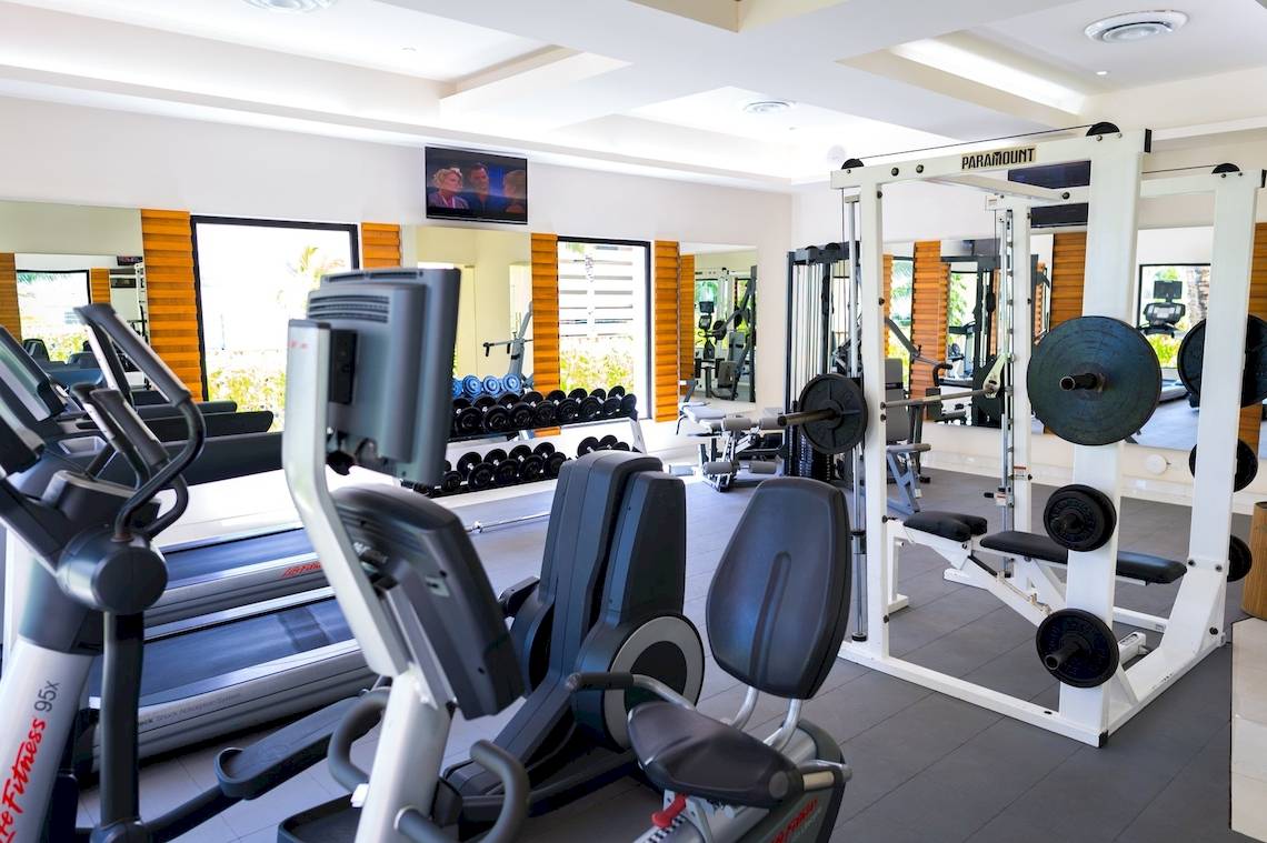 Fitnesscenter im The Reef Coco Beach Hotel mit verschiedenen Trainingsgeräten und Spiegeln.