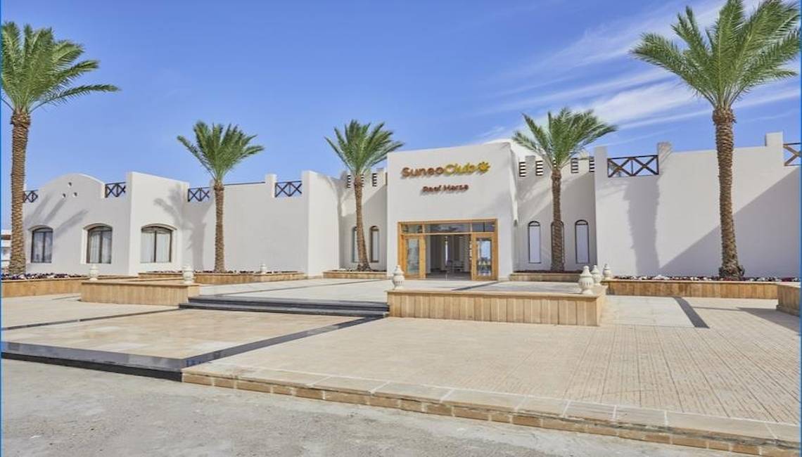Außenansicht des JAZ Neo Reef Marsa Hotels mit weißem Gebäude und Palmen.
