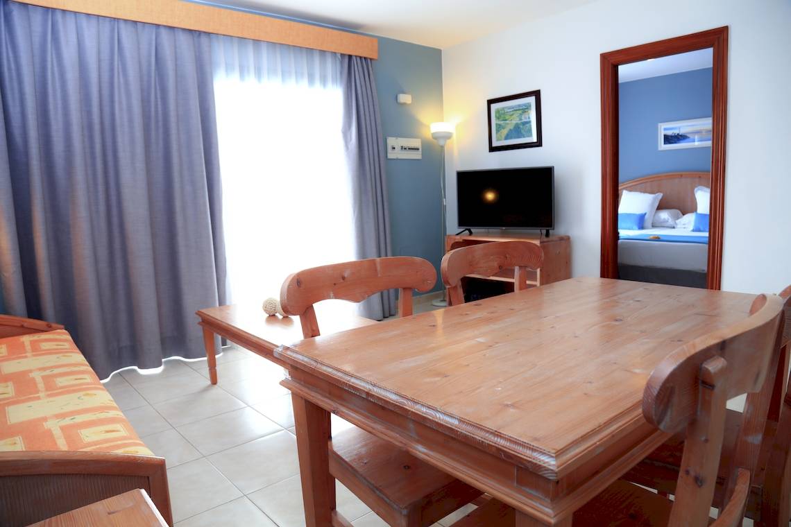 Innenansicht des Zimmers im Bluesea Aloe Corralejo Hotel mit Tisch, Stühlen, Fernseher und Schlafzimmerspiegel.