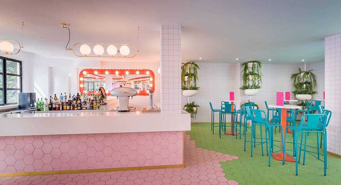 Innenansicht der Bar im Aparthotel Allegro Isora mit pinken und grünen Hexagon-Fliesen und blauen Stühlen.