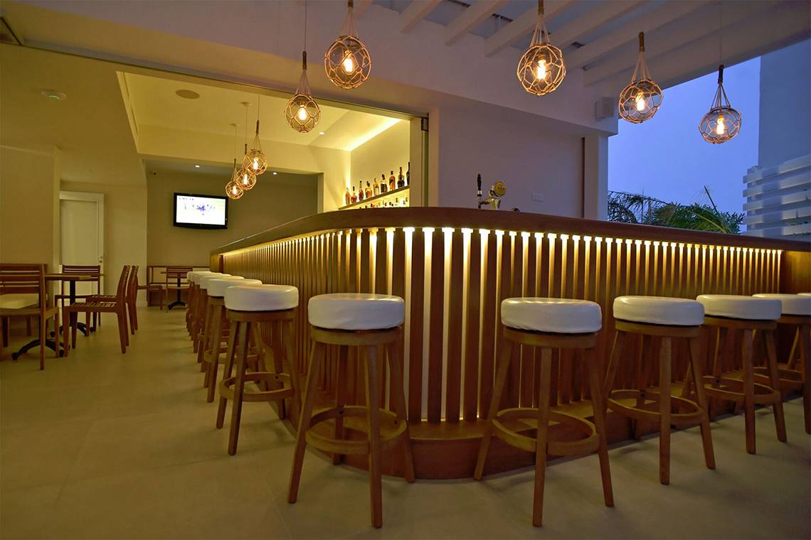 Bar im Sunrise Gardens Hotel mit Holzbar, Stühlen und Beleuchtung.