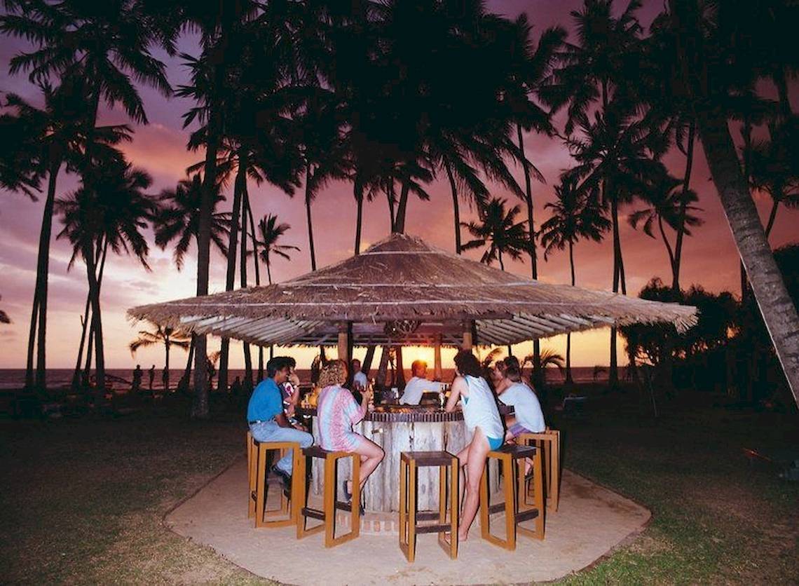 Gäste sitzen an einer Bar auf der Strandterrasse des Mermaid Hotel & Club bei Sonnenuntergang.