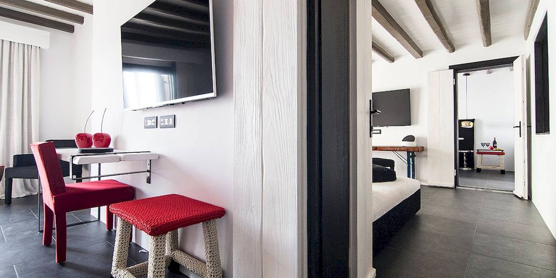 Hotelzimmer im Myconian Avaton Resort mit Fernseher an der Wand, rotem Stuhl und Tisch.