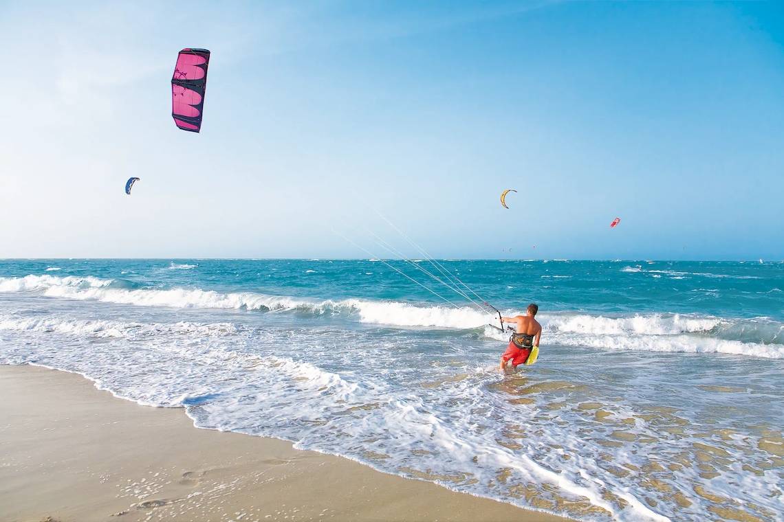 Ein Kitesurfer am Strand mit einer pinken Drachen im Himmel