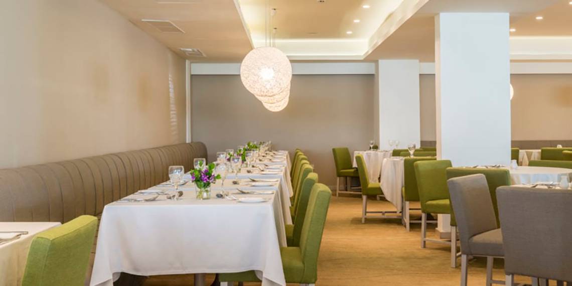 Innenbereich des Restaurants im Nissi Beach Resort mit langen Tischreihen und grünen Stühlen.