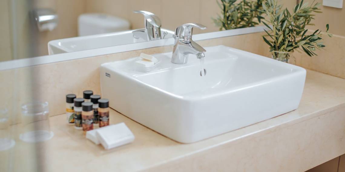 Badezimmer im Nissi Beach Resort mit einem weißen Waschbecken, Handtüchern und Toilette im Hintergrund.
