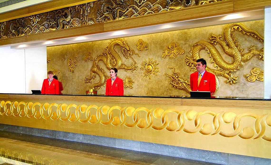 Rezeption des Royal Dragon Hotels mit goldenen Drachen-Wandverkleidungen und drei Mitarbeitern in roten Uniformen.