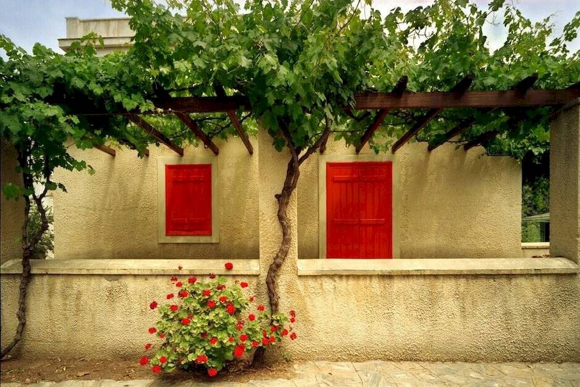 Außenansicht des Doryssa Seaside Resorts mit roten Fensterläden und blühenden roten Blumen.