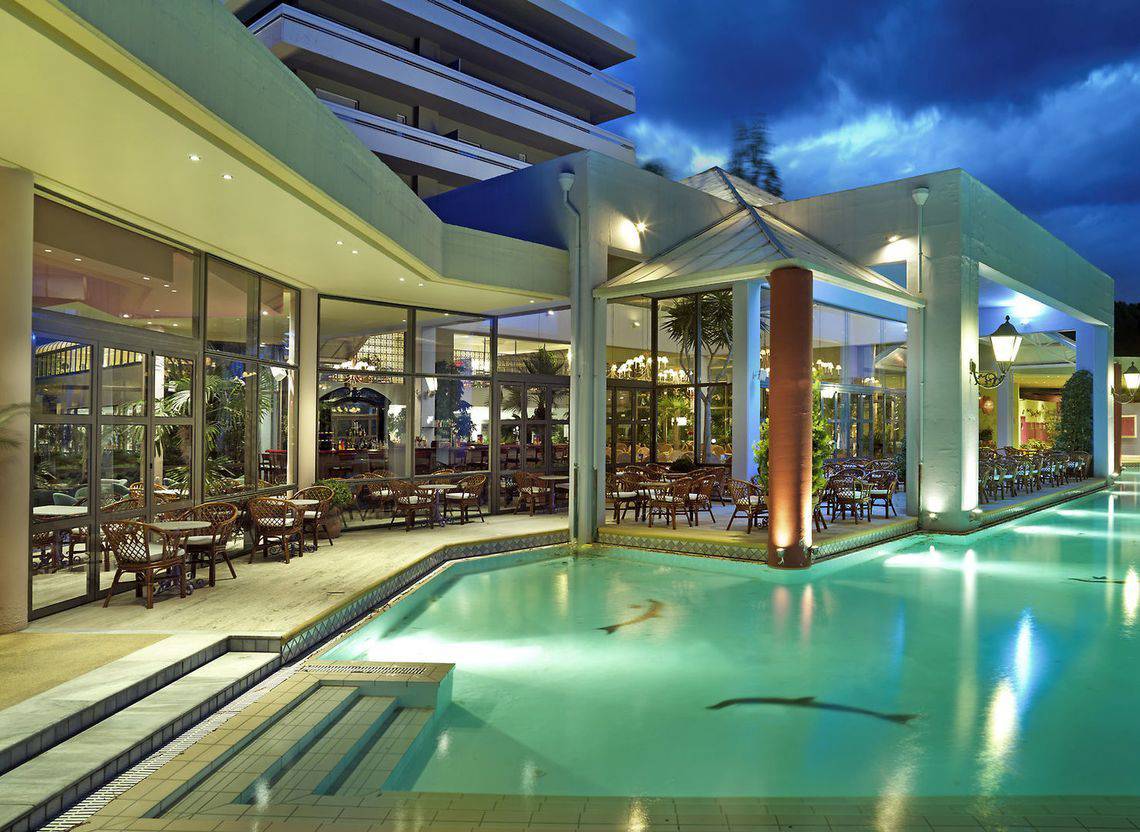 Außenbereich des Dionysos Hotels bei Nacht mit Pool und beleuchteten Tischen und Stühlen.