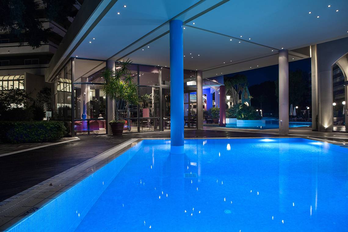 Außenbereich des Dionysos Hotels bei Nacht mit beleuchtetem Pool und moderner Architektur.