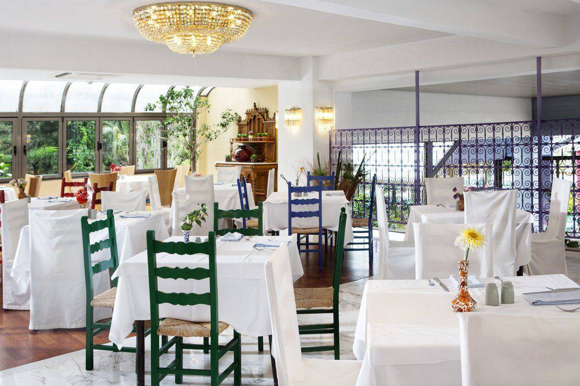 Innenbereich des Dionysos Hotels Restaurant mit weißen Tischen, grünen Stühlen und Kristallleuchtern.