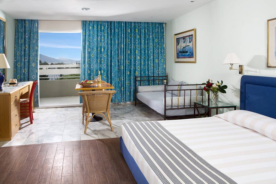 Innenansicht eines Zimmers im Dionysos Hotel mit Bett, Schlafsofa und Balkon.