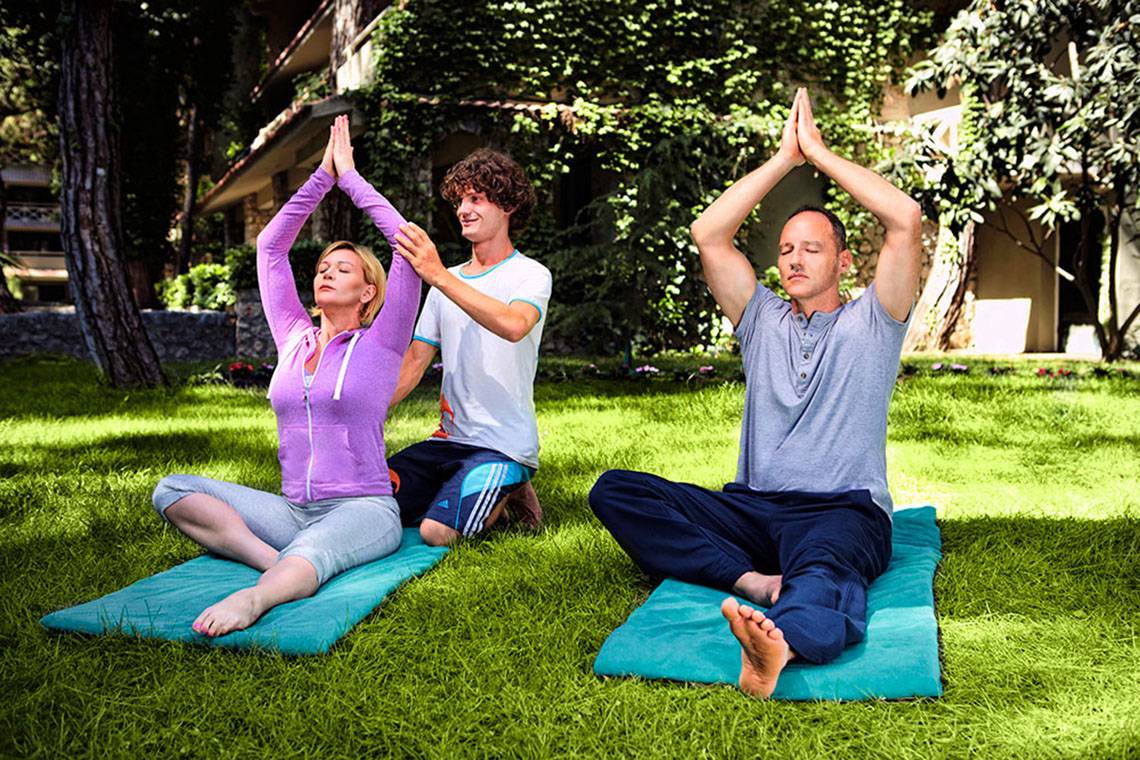 Drei Personen machen Yoga auf dem Rasen im Marti Myra Hotel.