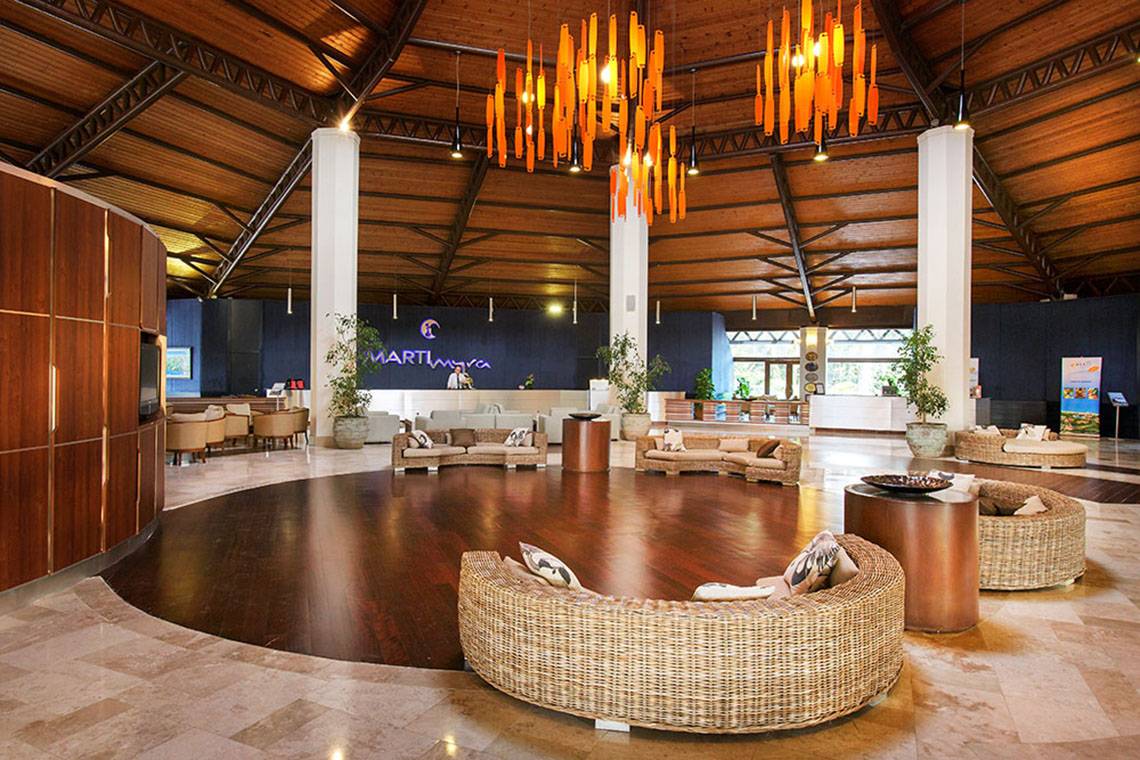 Hotellobby des Marti Myra mit Holzboden, Korbmöbeln und orangefarbenen Kronleuchtern.