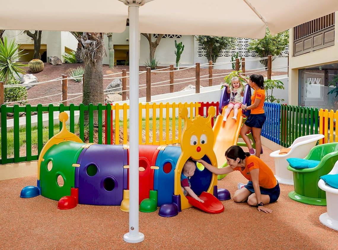 Kinderspielplatz im Freien im H10 Rubicon Palace Hotel mit bunten Spielgeräten und einer Frau, die ein Kind beobachtet.