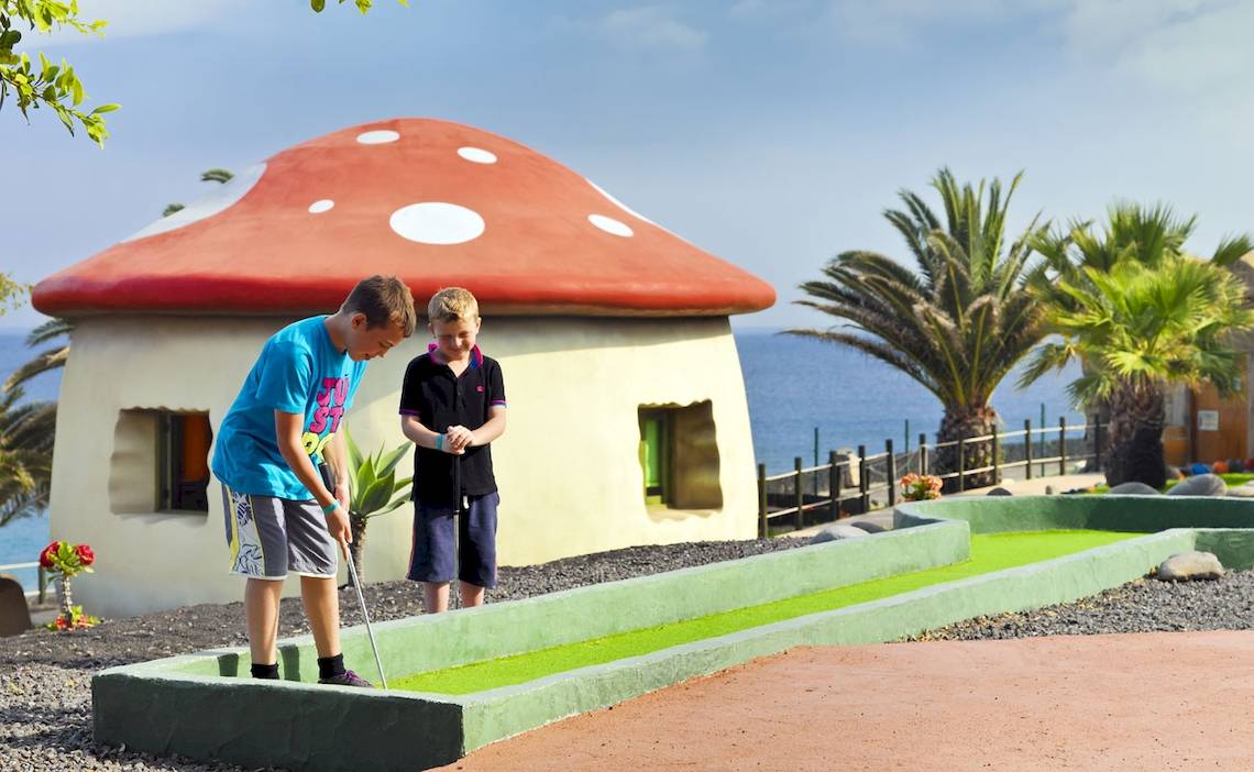 Zwei junge Jungs spielen Golf auf einem Pilzhaus-Golfplatz mit Meer im Hintergrund
