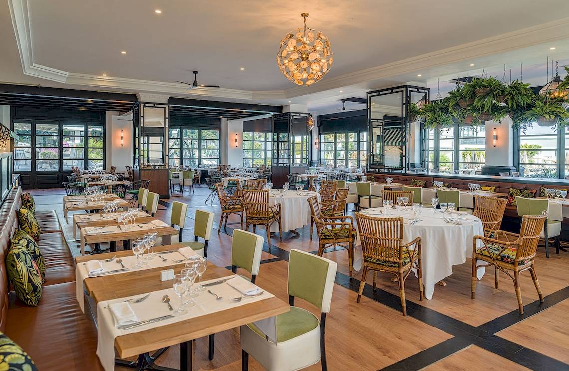 Innenbereich des H10 Rubicon Palace Restaurants mit Holztischen, Stühlen und einer großen Kronleuchter.