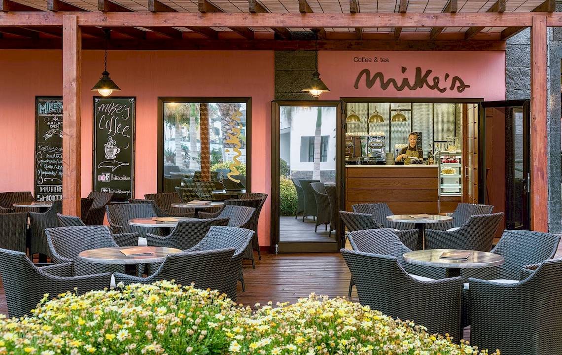 Innenbereich des Mike's Cafe im H10 Rubicon Palace Hotel mit Tischen und Stühlen.