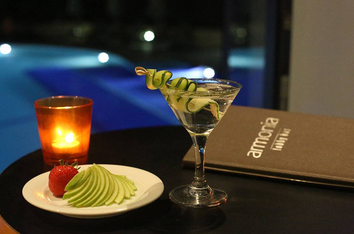 Cocktailglas mit Apfelscheiben und Erdbeere auf einer Platte neben einem Teelicht und einem Buch im Minos Mare Royal Hotel.