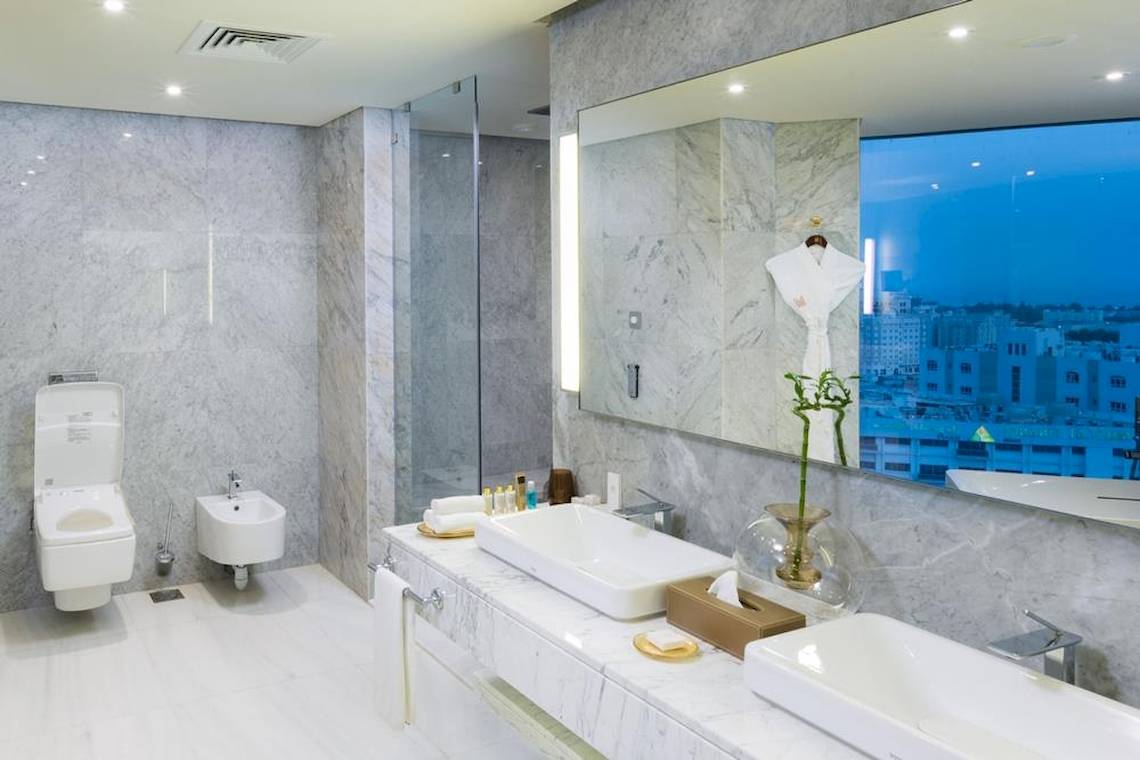 Luxuriöses Badezimmer im Grand Millennium Muscat Hotel mit Marmorwänden und Doppelwaschbecken.