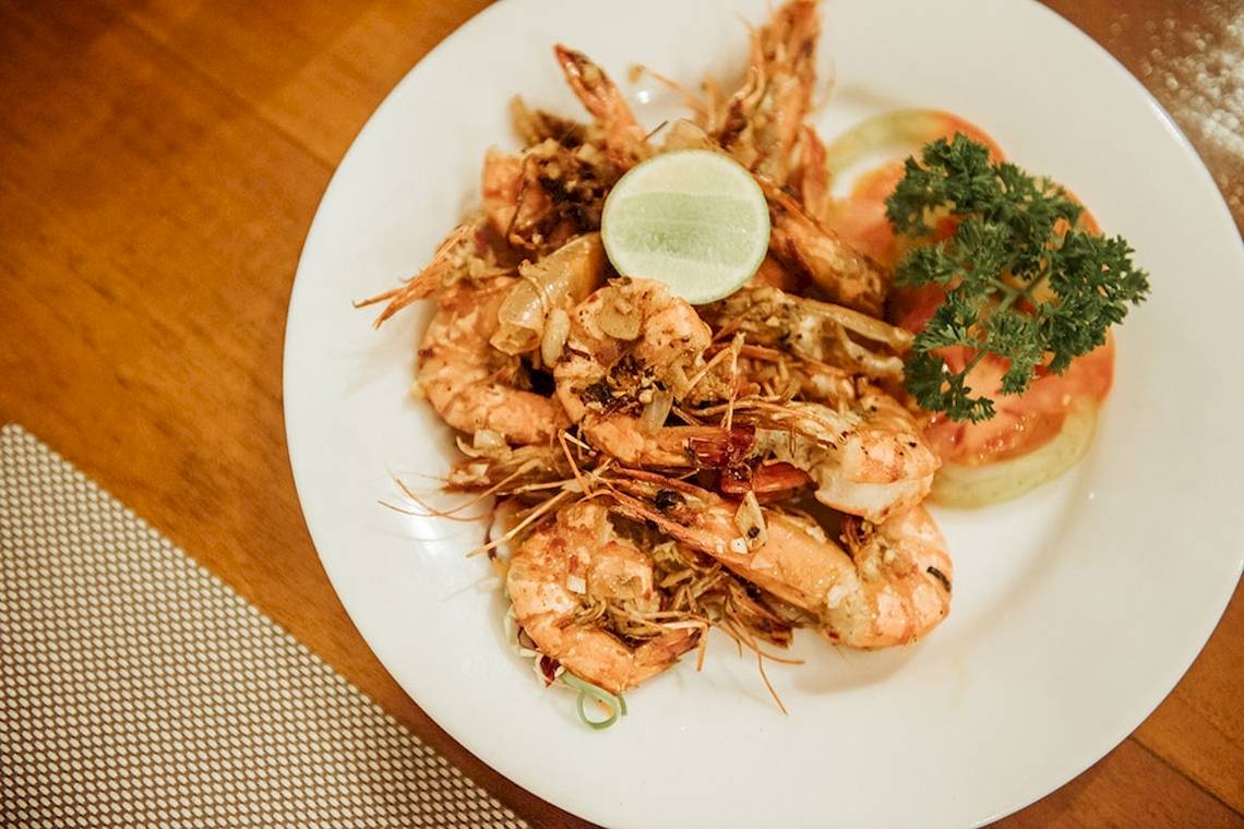 Ein weißer Teller mit gegrillten Garnelen, Tomatenscheiben und einer Limettenscheibe.