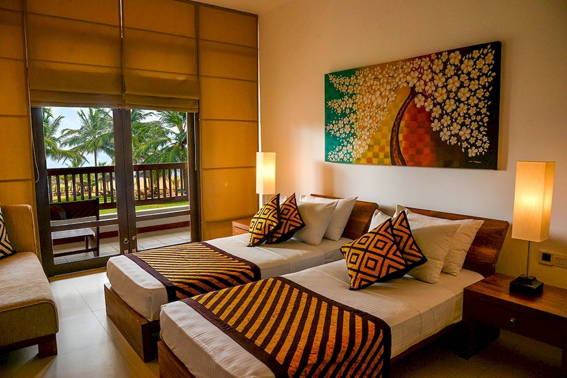 Zwei Betten im Zimmer im Goldi Sands Hotel mit Meerblick durch Glastüren.