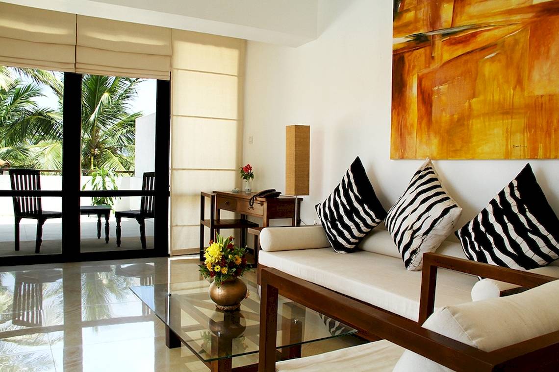 Wohnzimmer im Goldi Sands Hotel mit einem Sofa, Kissen, Tisch und Blick auf Palmen