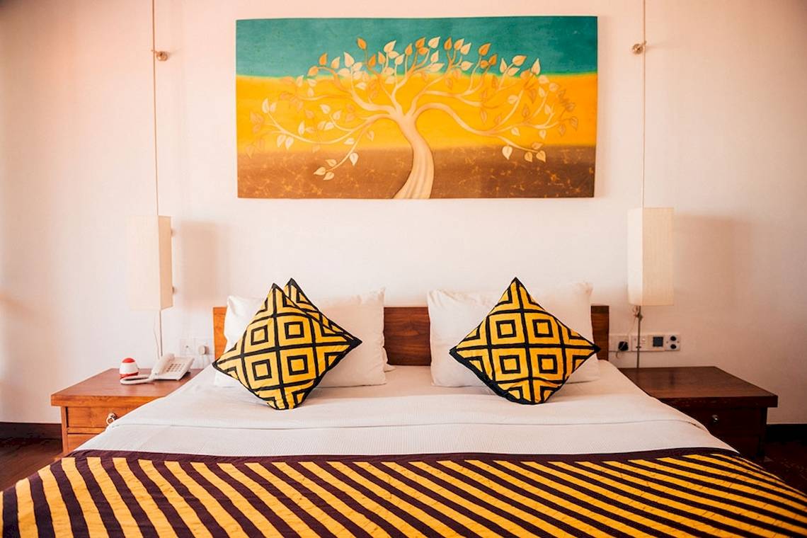 Goldi Sands Hotel Schlafzimmer mit Bett, Kissen und Wandmalerei.
