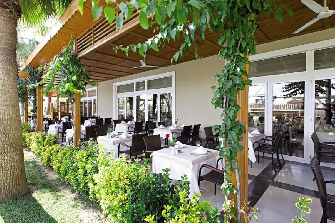 Restaurantbereich des Adalya Bliss Hotels mit Tischen und Stühlen unter einer überdachten Terrasse