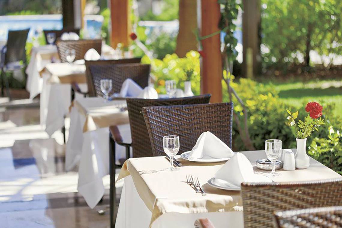Restauranttisch im Freien im Adalya Bliss Hotel, elegant gedeckt mit Pflanzen im Hintergrund.