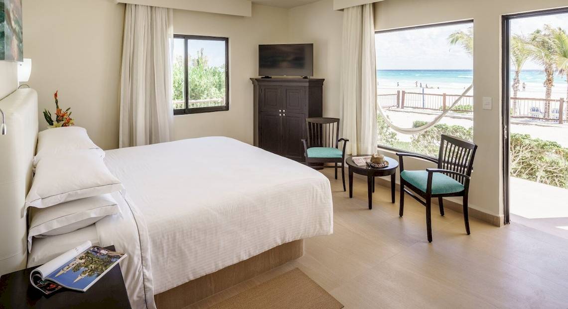 Innenansicht eines Hotelzimmers im Allegro Playacar mit Blick auf das Meer, inklusive Bett, Fernseher, Tisch und Stühlen.