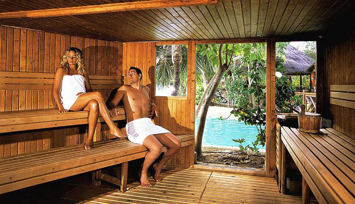 Ein Paar sitzt in einer Holzsauna mit einem Ausblick auf einen Pool.