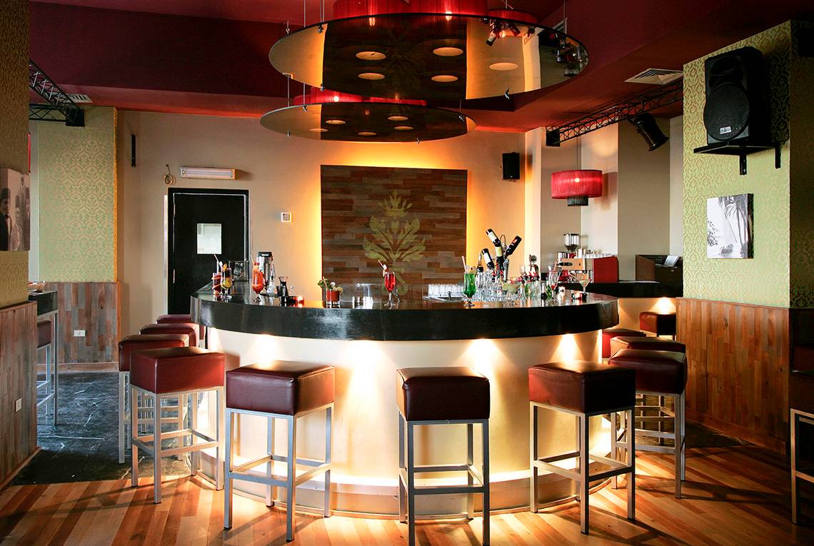 Bar im Three Corners Ocean View Hotel mit gepolsterten Stühlen und einer Theke voller Getränke.