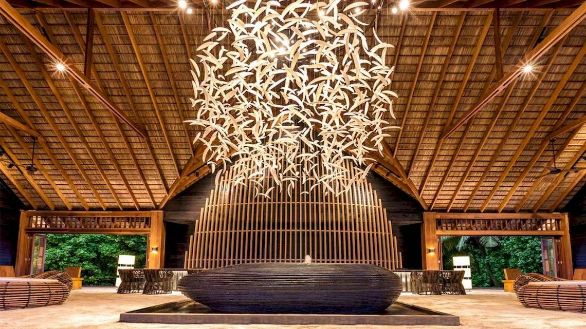 Lobby des Hurawalhi Island Resorts mit einer großen dekorativen Deckenlampe und Sitzgelegenheiten.