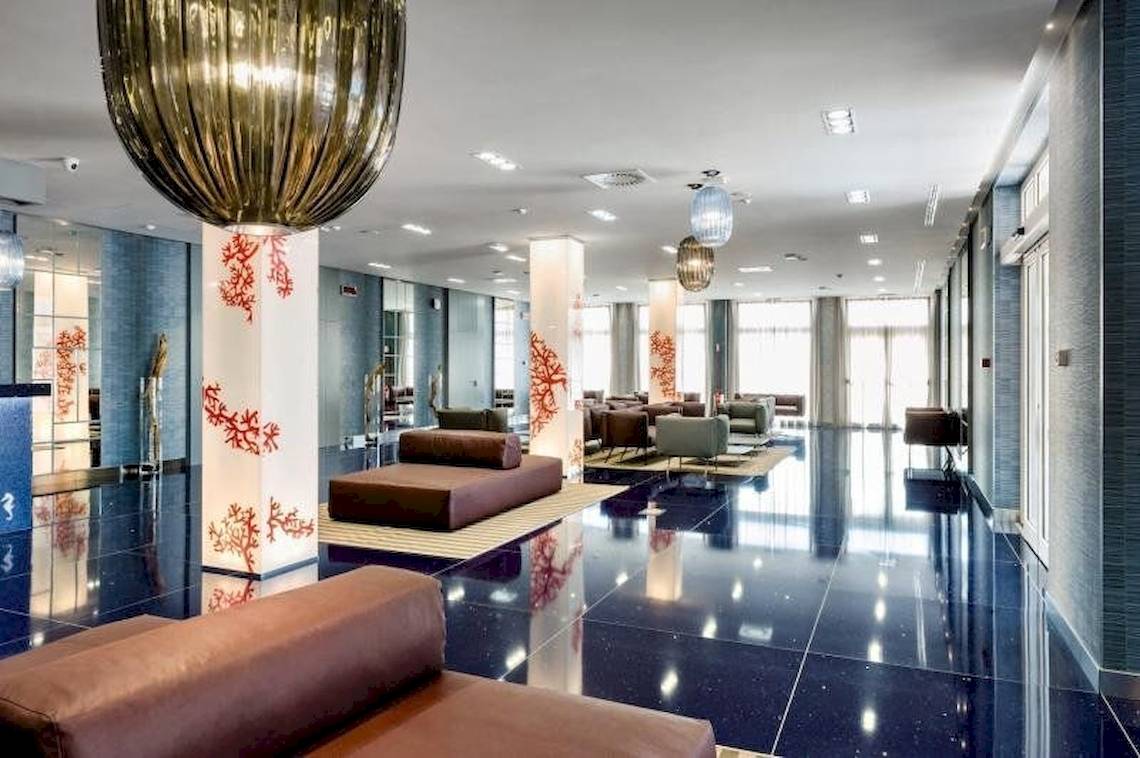 Lobby des Cala Ponte Hotels mit modernen Möbeln und einer großen Kronleuchter