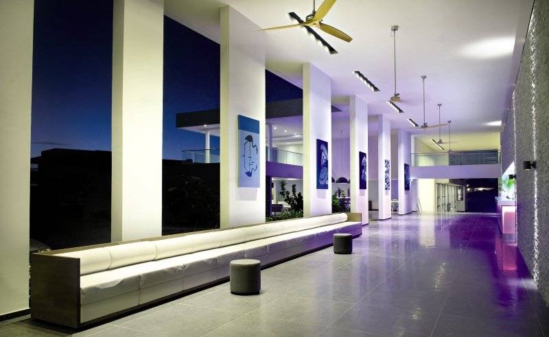 Der Eingangsbereich des Papagayo Beach Hotel & Resort mit einem langen weißen Sofa, violetten Boden und großen Kunstwerken an der Wand.
