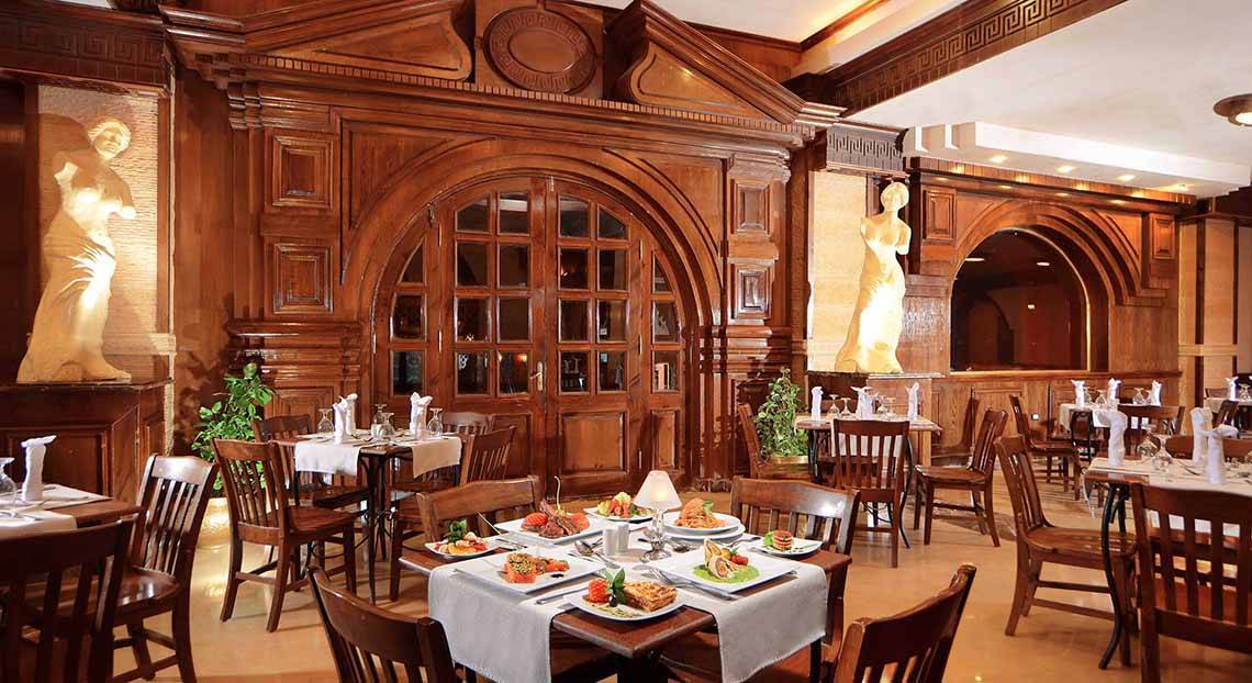 Innenansicht des Restaurants des Pickalbatros Alf Leila Wa Leila Resorts mit holzvertäfelten Wänden, Statuen und gedeckten Tischen.