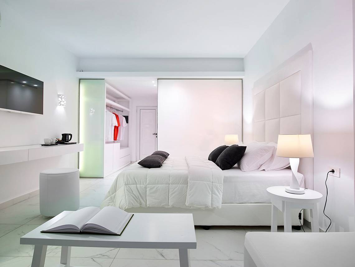 Ein modernes Schlafzimmer im Dimitra Beach Hotel & Suites mit weißen Wänden, einem großen Bett und Nachttischen.