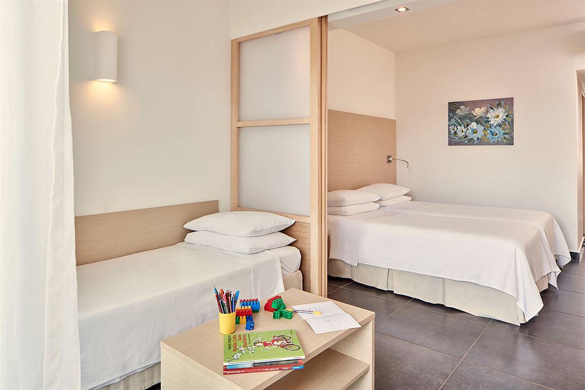 Schlafzimmer mit zwei Betten im Atlantica Mikri Poli Kos Hotel, mit Nachttischen, Büchern und Spielzeug.