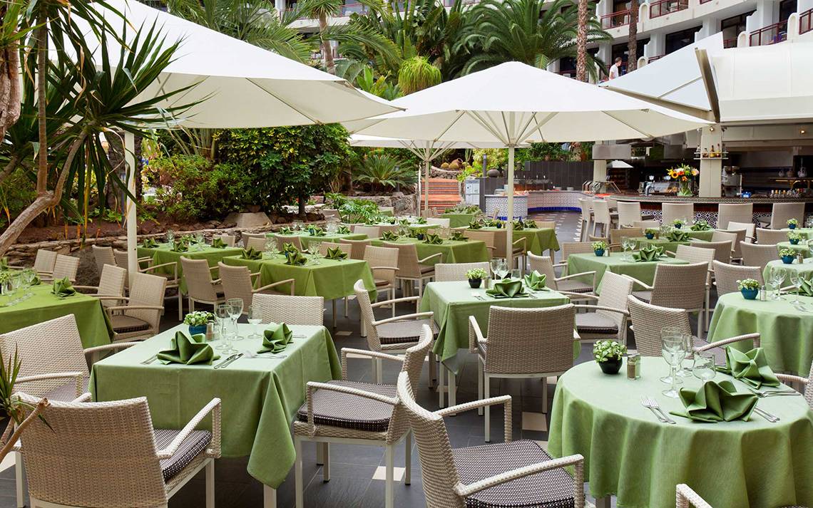 Außenbereich des Seaside Sandy Beach Hotels mit gedeckten Tischen und Stühlen unter Schirmen.