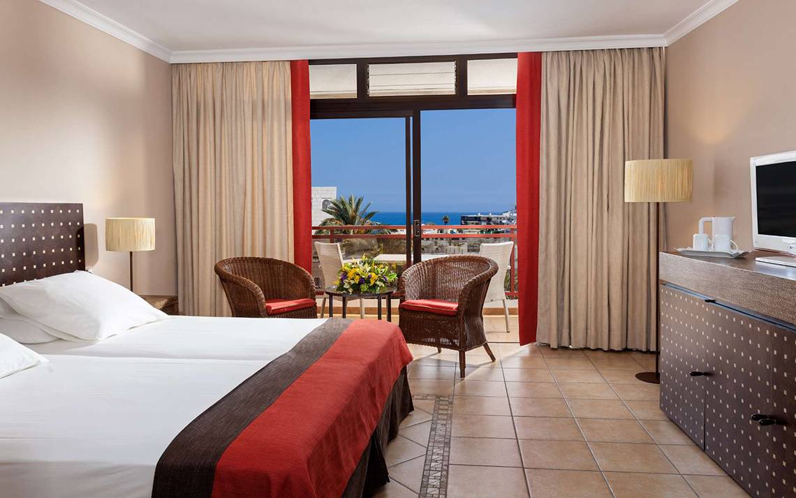 Doppelzimmer mit Meerblick im Seaside Sandy Beach Hotel, mit zwei Betten, zwei Korbstühlen und einem großen Fenster.