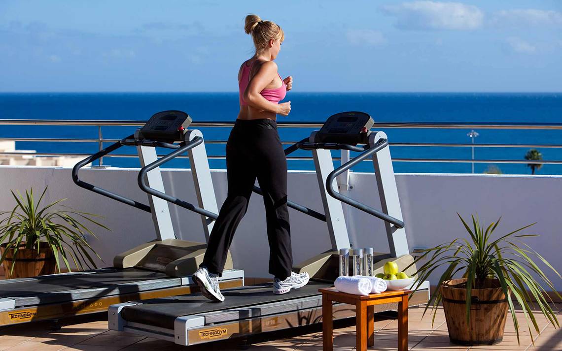 Frau läuft auf einem Laufband auf der Terrasse mit Blick auf das Meer.