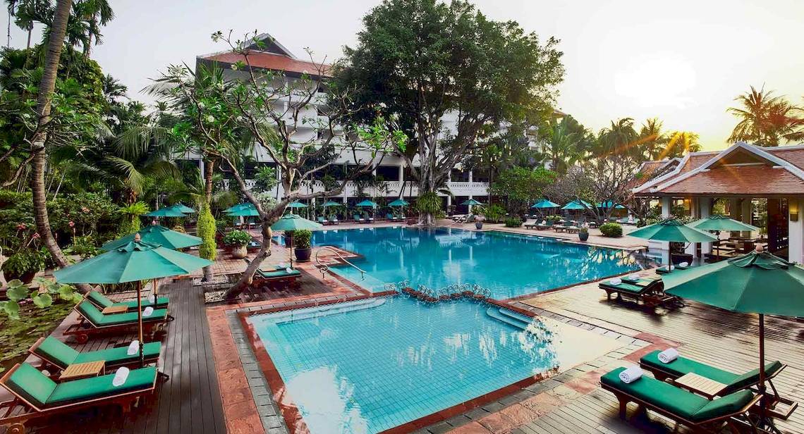 Außenbereich des Anantara Riverside Bangkok Resort mit Swimmingpool, grünen Sonnenschirmen und Liegestühlen.