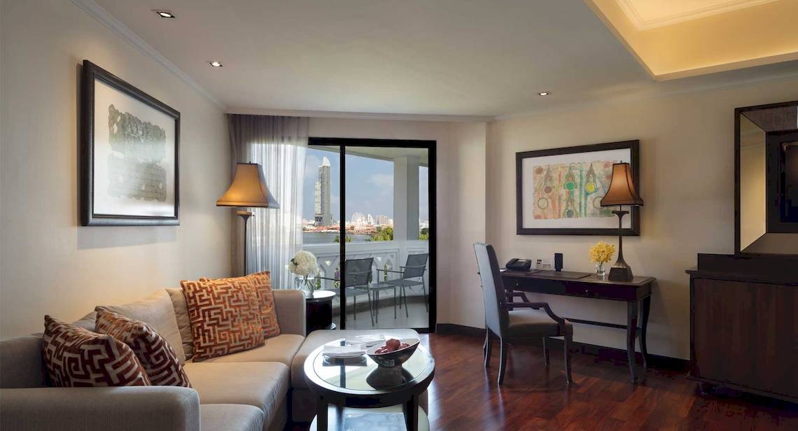 Wohnbereich des Anantara Riverside Bangkok Resorts mit Sofa, Tisch, Schreibtisch und Balkon.