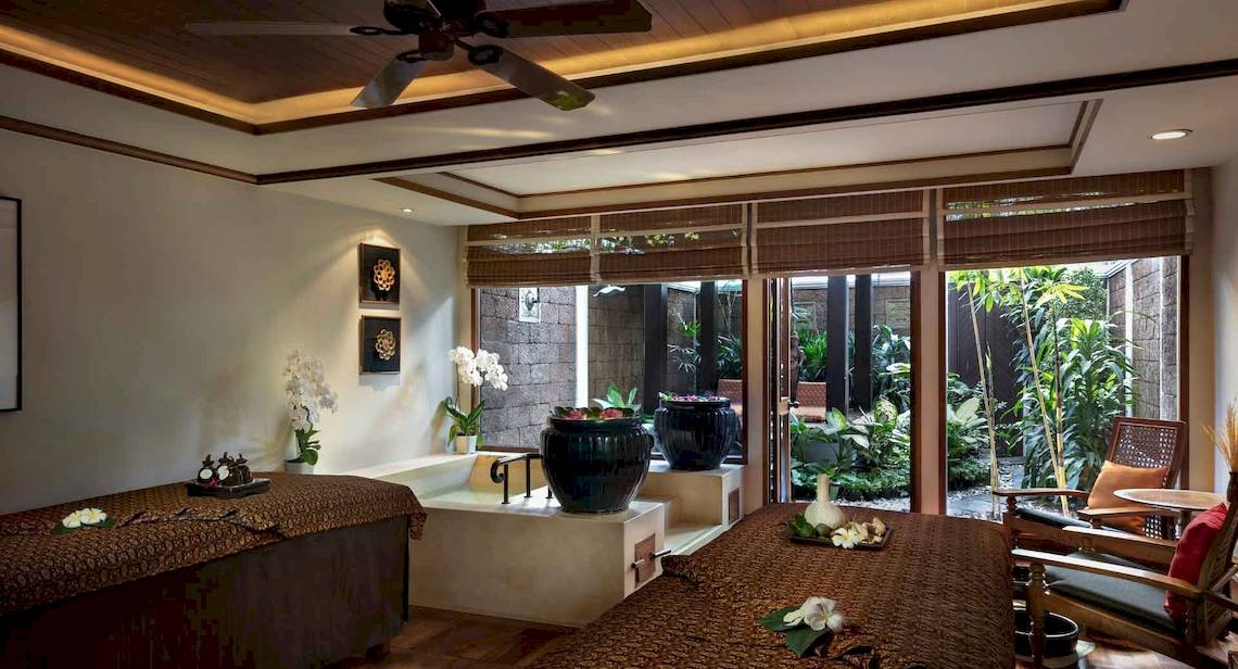 Spa-Behandlungsraum im Anantara Riverside Bangkok Resort mit zwei Betten, einem Whirlpool und Pflanzen im Hintergrund.