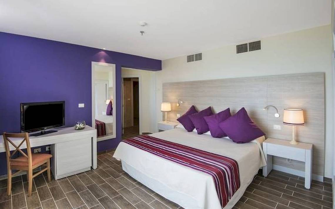 Blau Varadero Hotelzimmer mit violetten Wänden, Bett und Fernseher.
