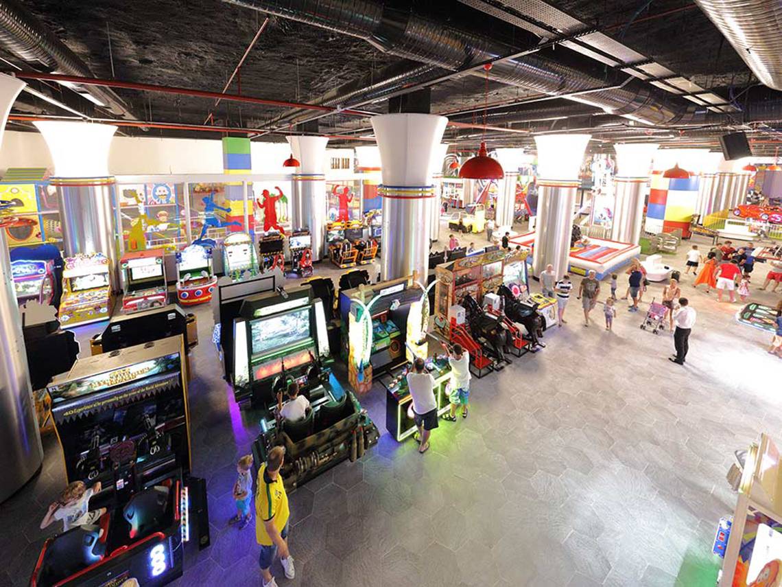 Übersicht über die Spielhalle im Sueno Hotels Deluxe Belek mit verschiedenen Arcade-Spielen und Gästen, die spielen und herumlaufen.
